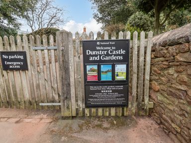 A wooden picket fence with signs for Dunster Castle and Gardens and no parking emergency access in Dunster