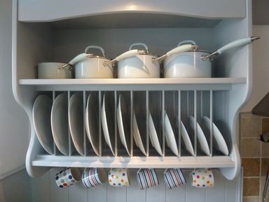 A kitchen rack with white pots on the top shelf white plates on the middle rack and colorful mugs hanging underneath at Bodkin Cottage in Dunster