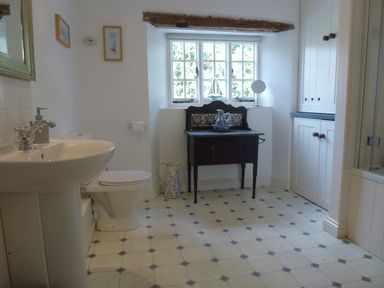 A bathroom with a sink toilet a dark wooden cabinet under a window and built in cupboards at Bodkin Cottage in Dunster