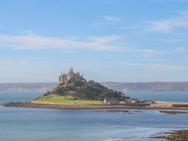 An island with a castle on top surrounded by water and land in the background at Driftwood in Marazion