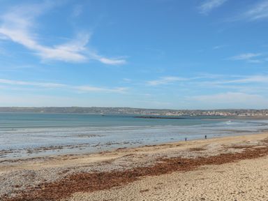 A beach with seaweed on the sand and a calm ocean with a town visible in the distance Driftwood Marazion