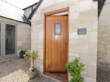 An open wooden front door on a stone building with potted plants and a sign reading The Nook at Jack's Green near Painswick