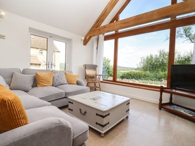 A living room with a gray sofa yellow pillows a white coffee table large window with wooden frame and a wooden chair at The Nook in Jack's Green near Painswick