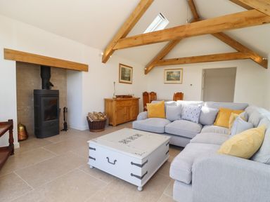 A living room with a grey sectional sofa with pillows a white coffee table wooden beams and a wood stove at The Nook in Jack's Green near Painswick