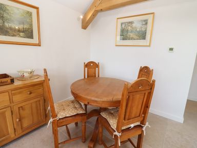 A dining area with a round wooden table and four wooden chairs with cushions and a wooden sideboard with a bowl and a wooden crate on it at The Nook in Jacks Green near Painswick