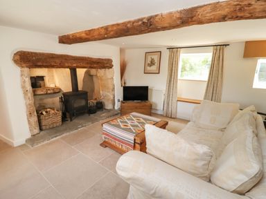 A living room with a wood stove fireplace a wooden coffee table a patterned rug a television and a sofa at The Nook in Jack's Green near Painswick