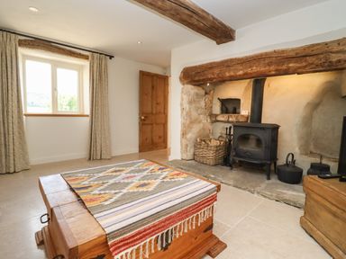 A room with a wood burning stove a wooden chest with a woven cloth a window with curtains and a wooden door at The Nook in Jack's Green near Painswick