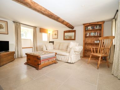 A living room with a wooden coffee table a white sofa a wooden bookshelf and a wooden chair at The Nook Jack's Green near Painswick