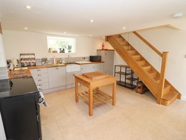 A kitchen with wooden countertops a black oven a wooden island and a wooden staircase at The Nook in Jack's Green near Painswick