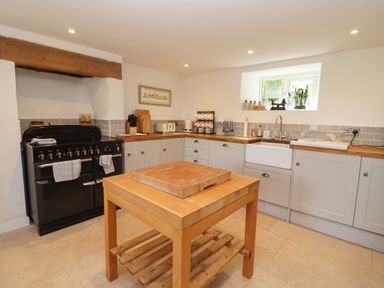 A kitchen with a wooden island table a black oven and grey cabinets with wooden countertops at The Nook in Jack's Green near Painswick
