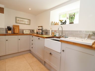 A kitchen with wooden countertops white cabinets a sink a dish rack and kitchen utensils at The Nook in Jack's Green near Painswick