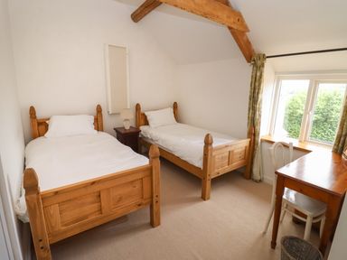 A bedroom with two single wooden beds a wooden desk a chair and a window with curtains at The Nook in Jacks Green near Painswick