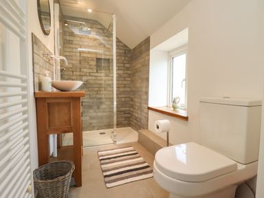 A bathroom with a toilet a wooden sink cabinet a glass shower enclosure and a window at The Nook Jack's Green near Painswick
