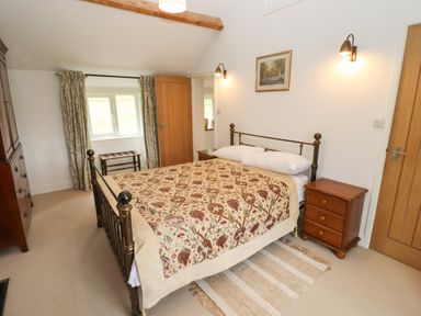 A bedroom with a metal bed frame wooden nightstands a wooden dresser a window with curtains and two doors at The Nook in Jack's Green near Painswick