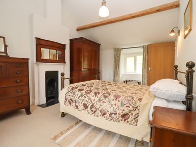A bedroom with a patterned bedspread wooden furniture and a fireplace at The Nook Jack's Green near Painswick
