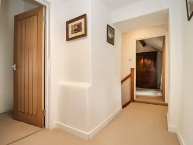 A hallway with beige carpet wooden doors and framed pictures on white walls at The Nook in Jack's Green near Painswick