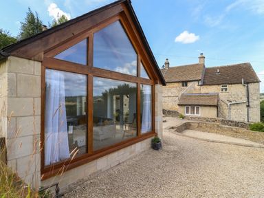 A stone house with large wooden framed windows and gravel driveway at The Nook in Jacks Green near Painswick