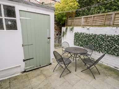 A small outdoor patio with a round metal table and four matching chairs near a green door and white walls with trellis at 89 Caledonia Street Scarborough
