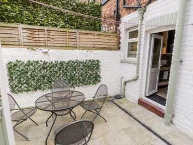 A small outdoor patio area with metal table and chairs against white brick walls with greenery at 89 Caledonia Street in Scarborough