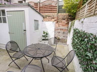 An outdoor patio with a round metal table and four matching chairs next to a small shed and a brick wall with a small gate 89 Caledonia Street Scarborough