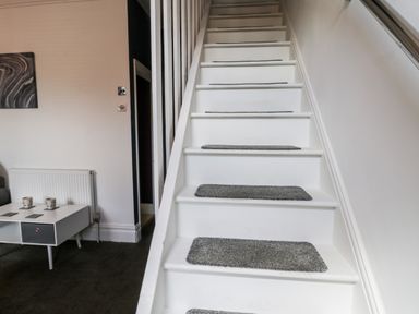 A white staircase with gray stair treads next to a living area with a white table and a radiator at 89 Caledonia Street in Scarborough