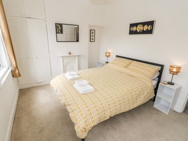 A bedroom with a bed with yellow patterned bedding two bedside tables with lamps a window with curtains and a wardrobe at 89 Caledonia Street in Scarborough