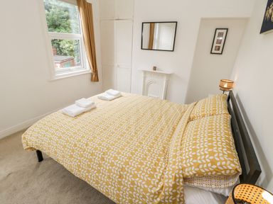 A bedroom with a bed with yellow patterned bedding towels folded on bed beside a window with brown curtains a wardrobe a wall mirror and a small lamp at 89 Caledonia Street in Scarborough