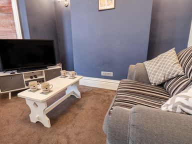 A living room with a striped sofa a white coffee table with four mugs a television and a media unit at 89 Caledonia Street in Scarborough