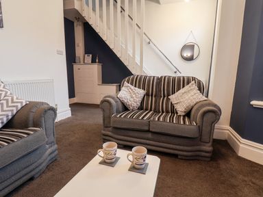 A living room with two striped sofas a white table with two mugs under stairs with a round mirror at 89 Caledonia Street in Scarborough