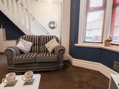 A seating area with a striped sofa two cushions a white table with two mugs a bay window with blinds and flowers at 89 Caledonia Street in Scarborough