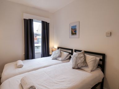 A bedroom with two single beds with white bedding and rolled towels near a window with dark curtains at 89 Caledonia Street in Scarborough
