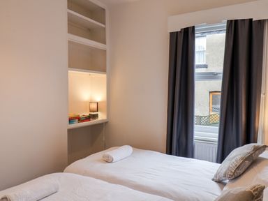 A bedroom with two single beds each with a rolled towel a built-in shelf with books and a lamp and a window with dark curtains at 89 Caledonia Street in Scarborough