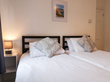A bedroom with two single beds bedside table and lamp with a framed Scarborough print on wall at 89 Caledonia Street in Scarborough