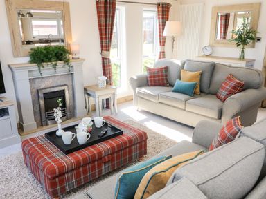 A living room with sofas cushions plaid ottoman and fireplace at Curlew Lodge in Carnforth