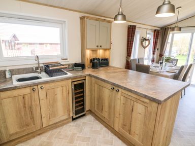 A kitchen with wooden cabinets a sink a wine cooler and a dining table with chairs at Curlew Lodge in Carnforth