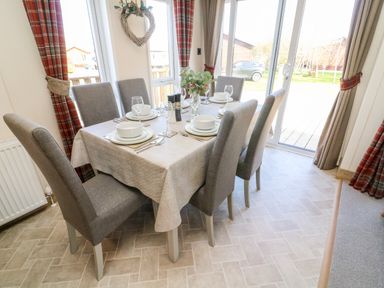 A dining area with a six seat table set with plates and glasses near sliding glass doors at Curlew Lodge in Carnforth