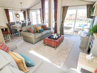 A living room with sofas a plaid ottoman and a dining area in the background at Curlew Lodge Carnforth