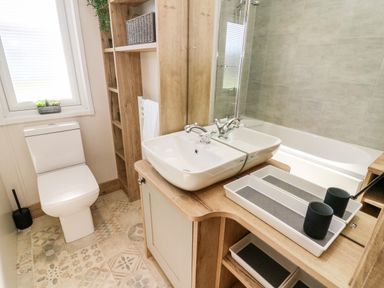 A bathroom with a toilet a sink a bathtub and wooden shelving at Curlew Lodge in Carnforth