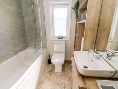 A bathroom with a bathtub shower toilet sink wooden shelving and a window at Curlew Lodge in Carnforth