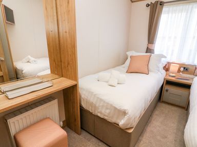 A bedroom with two single beds a bedside table with lamp and a wooden dressing table with a stool at Curlew Lodge in Carnforth