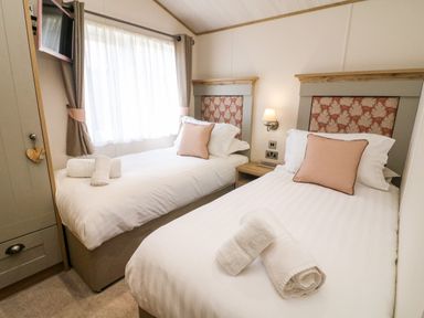 A bedroom with two single beds and rolled towels at Curlew Lodge in Carnforth
