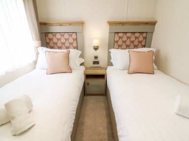 A bedroom with two single beds with pillows and towels separated by a nightstand with a lamp at Curlew Lodge in Carnforth