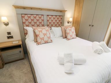 A bedroom with a double bed decorative pillows bedside tables wall lamps and folded towels at Curlew Lodge in Carnforth