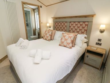 A bedroom with a double bed towels on the bed bedside table and an en suite bathroom at Curlew Lodge in Carnforth