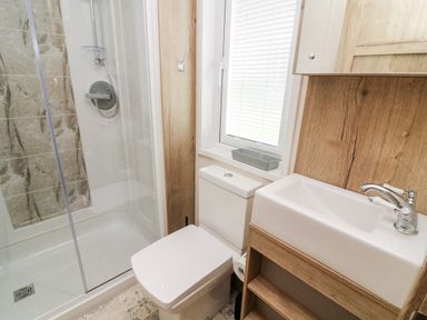 A bathroom with a shower, toilet, sink, and window at Curlew Lodge in Carnforth