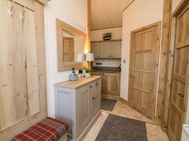 A hallway with wooden doors a cabinet mirror coat hooks and a bench at Curlew Lodge Carnforth