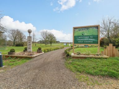 An entrance to caldecott hall golf course with a gravel path green grass and trees in fritton