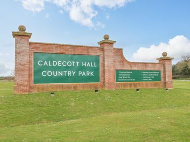 A brick wall sign with green panels reading Caldecott Hall Country Park on grass with sky background at Audrey's Lodge Foxburrow Hang in Fritton