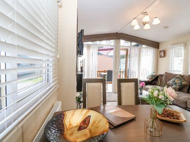A dining table with a decorative bowl a flower vase and menu cards in a living room with a sofa and glass doors at Audrey's Lodge Foxburrow Hang in Fritton
