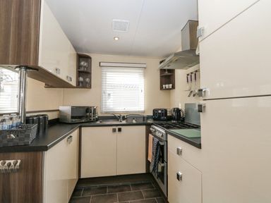 A kitchen with cabinets a stove a microwave toaster and kettle at Audrey's Lodge Foxburrow Hang in Fritton